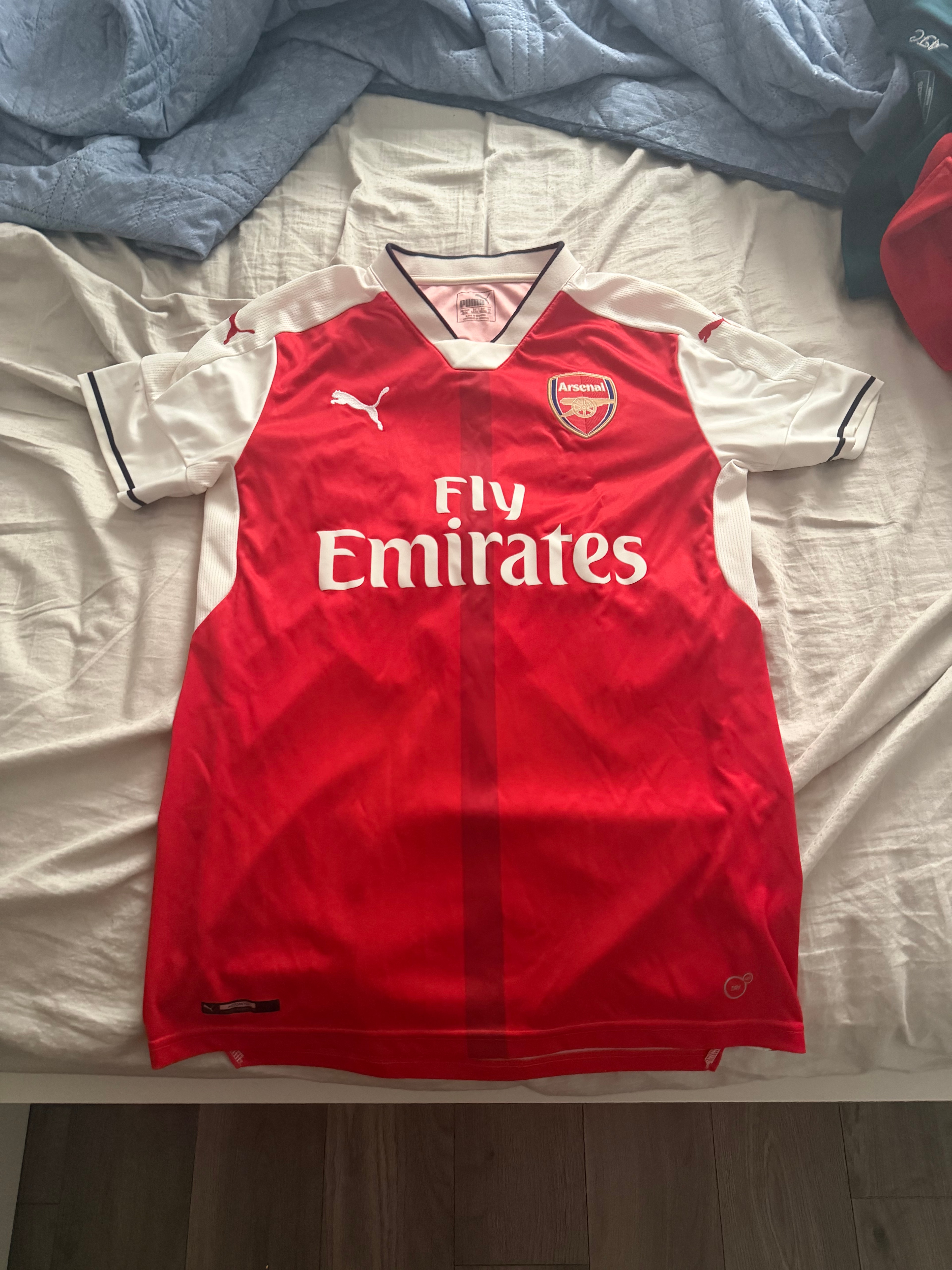 Shaaf's red and white Arsenal home jersey laid out on a bed.