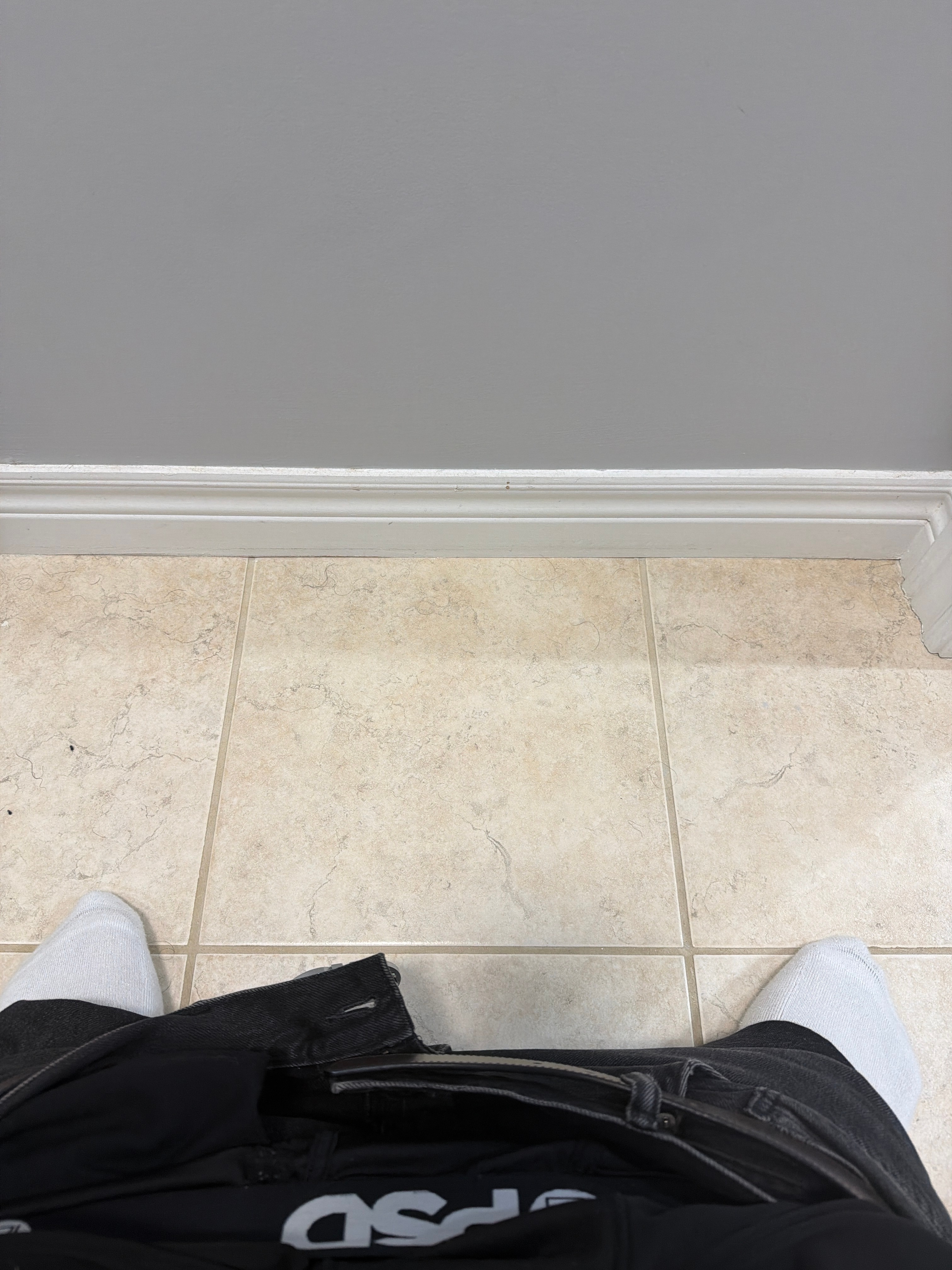 Shaaf's shoes facing a grey restroom wall and tiled floor.