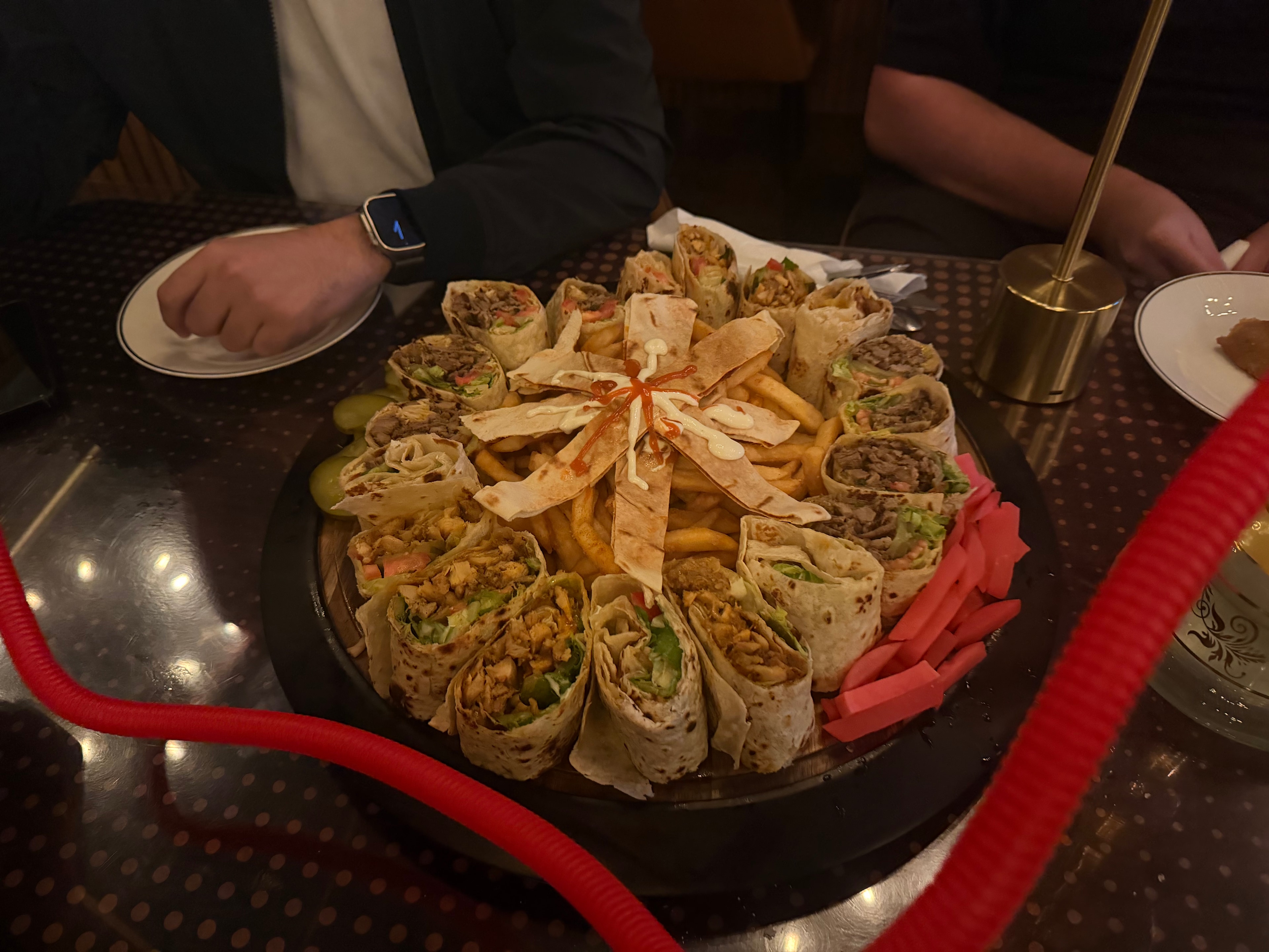 A large platter of shawarma wraps, fries, pickles, and sauces.